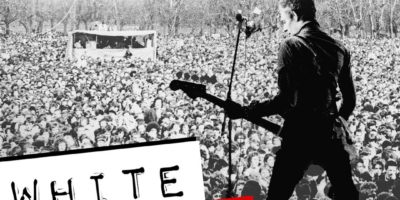 White Riot poster featuring grainy b&w image of Paul Simonon from The Clash playing in front of a crowd at Rock Against Racism's 1978 concert. photo ©Syd Shelton